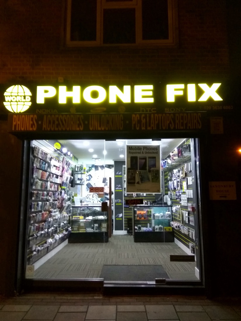 The World Phone Fix shopfront lit up at night, the yellow Phone Fix sign glowing over the display window.